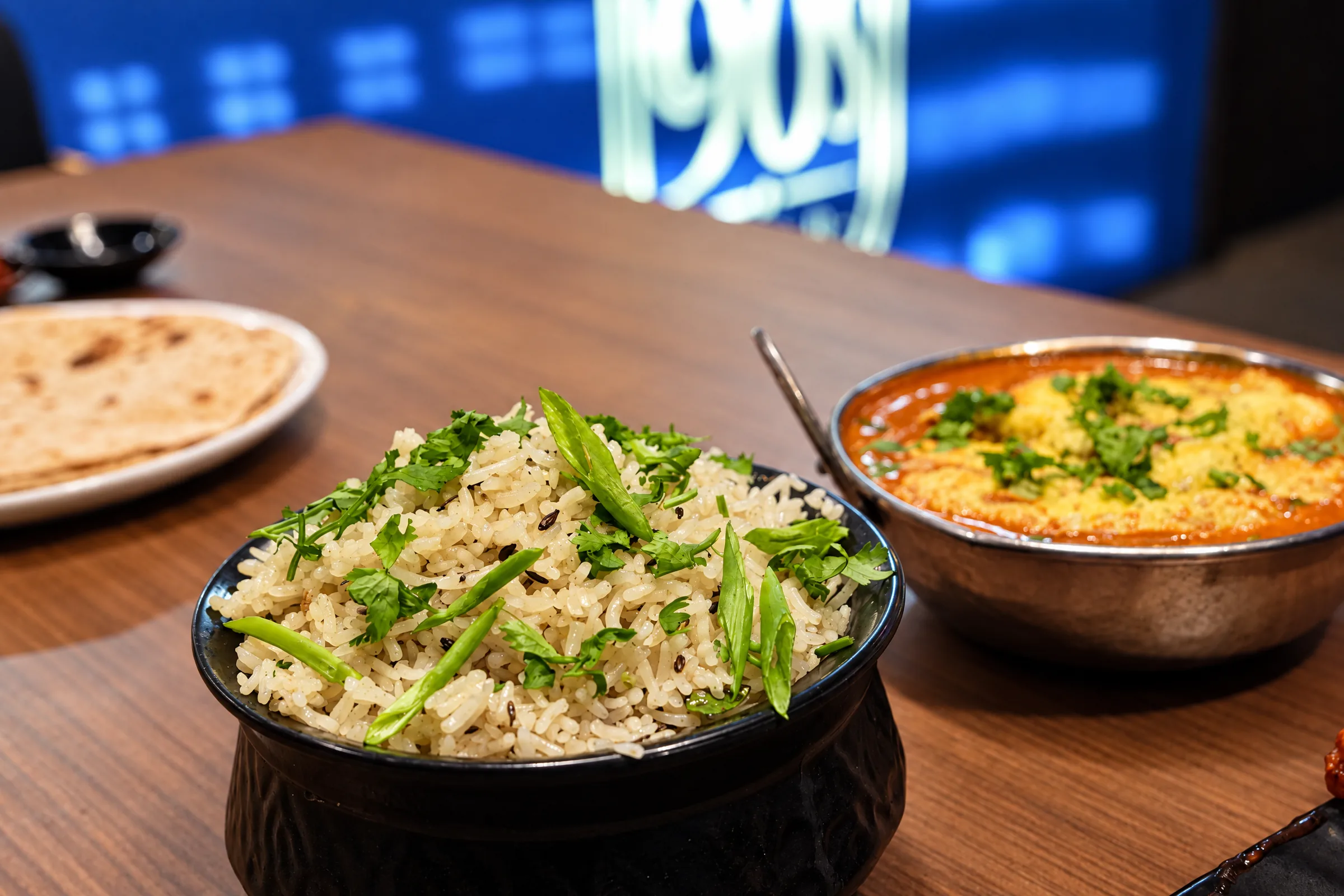 A bowl of biryani topped with spring onion, served with a curry and flatbread at The 90s Club.