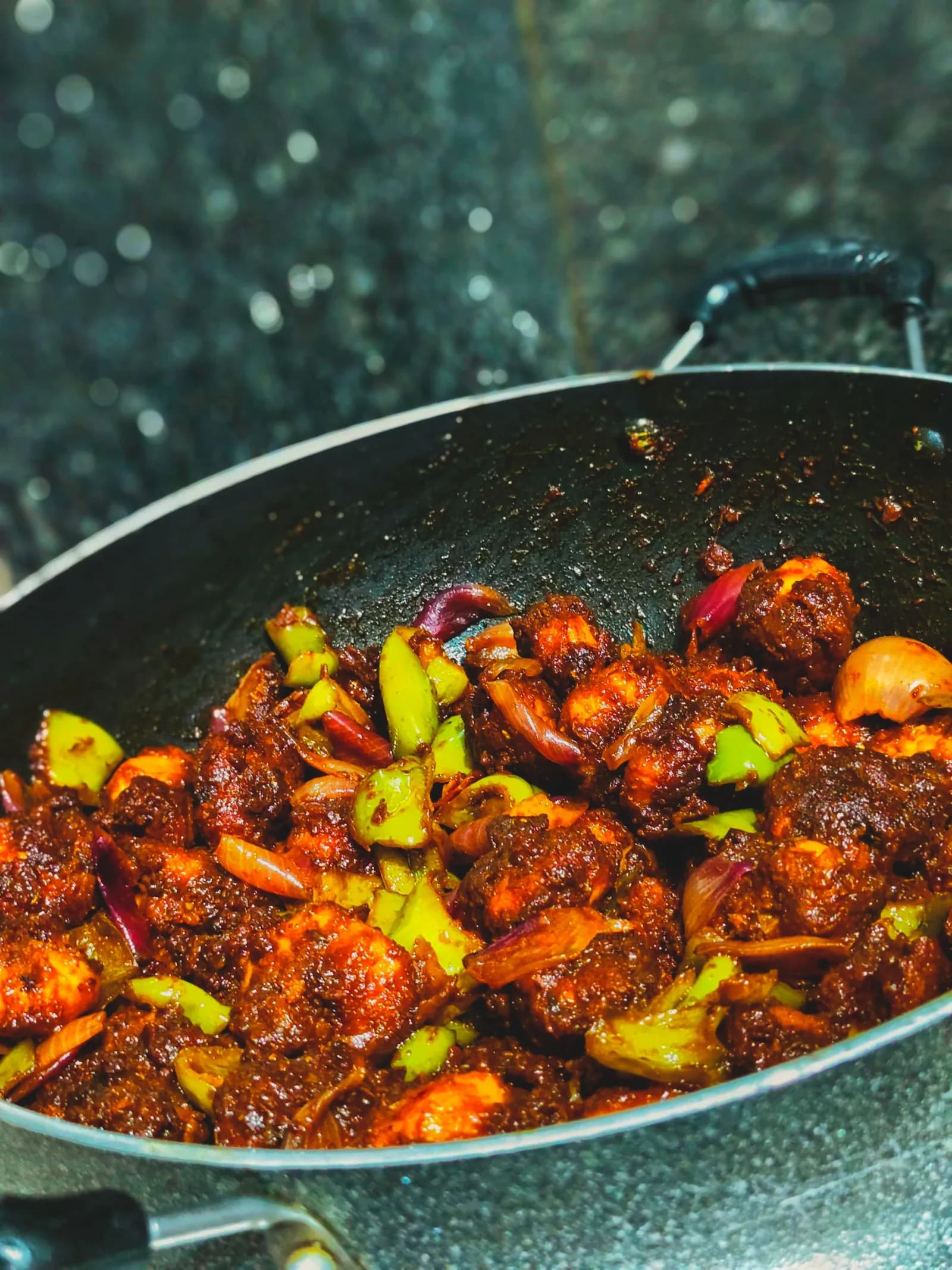 Prawns roasted in a dark red masala with green chillies in a steel kadai.