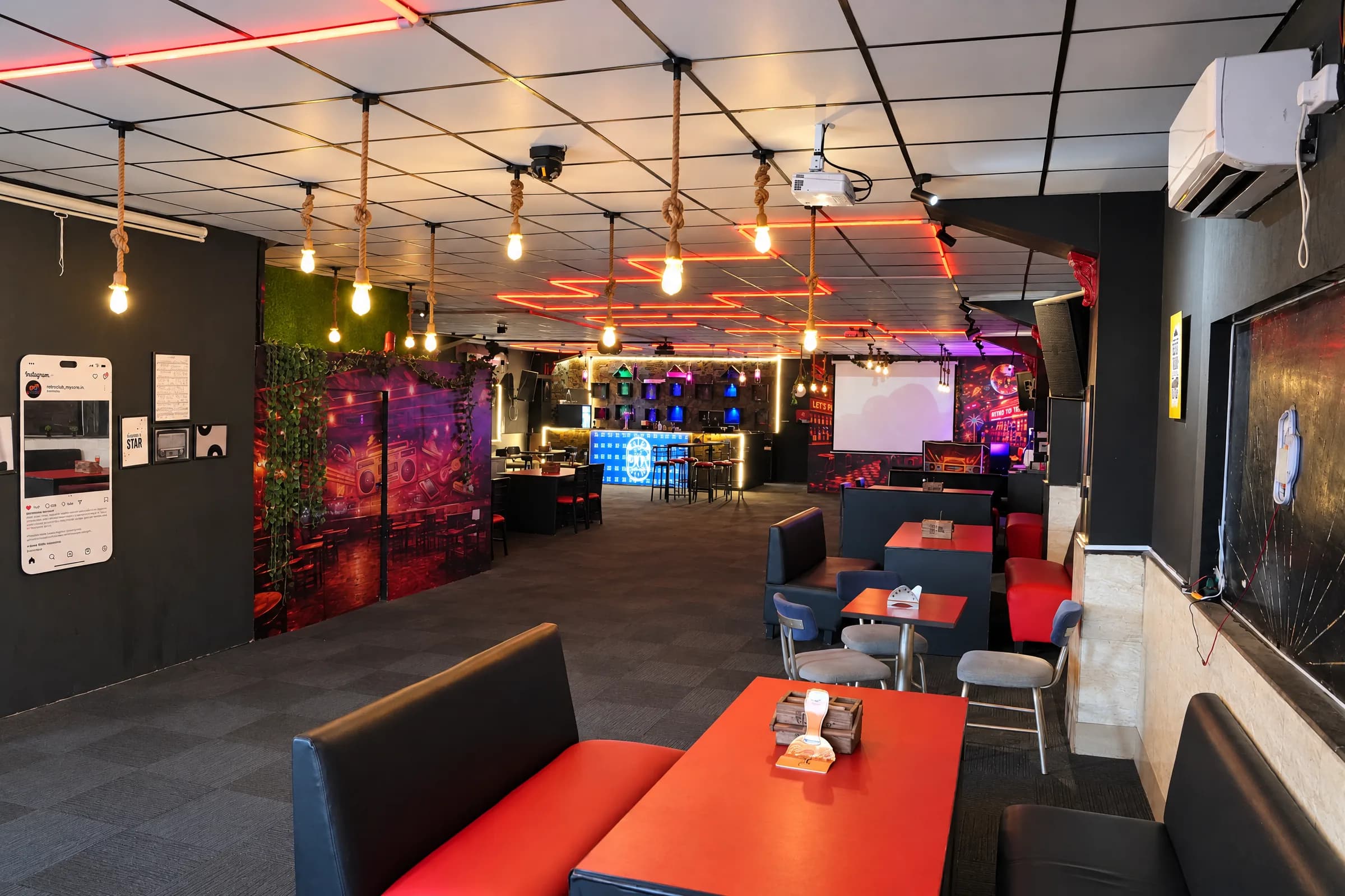 Booth seating with orange tables under hanging bulbs at The 90s Club, Electronic City.